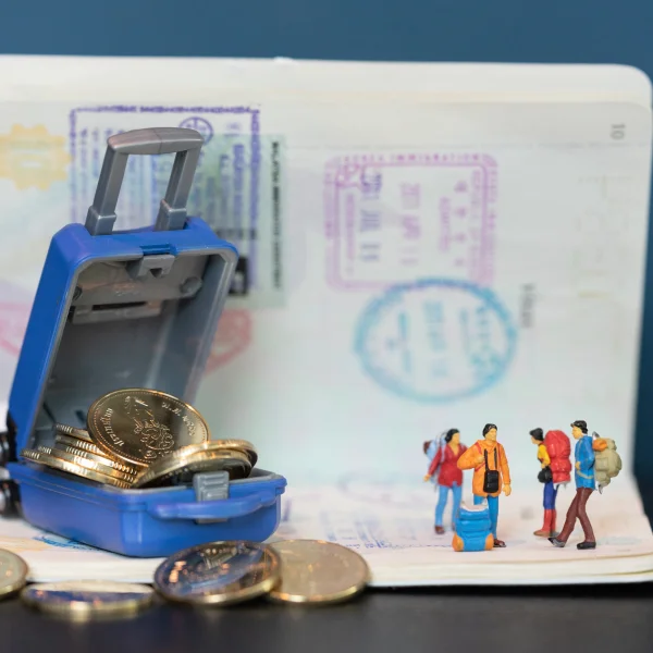 Miniature figures beside a suitcase filled with coins on a passport, symbolizing travel loans and financial planning for trips.