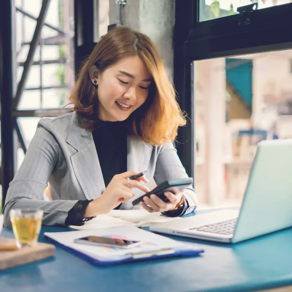 A woman at a table using a laptop and cell phone, available for loans seven days a week.