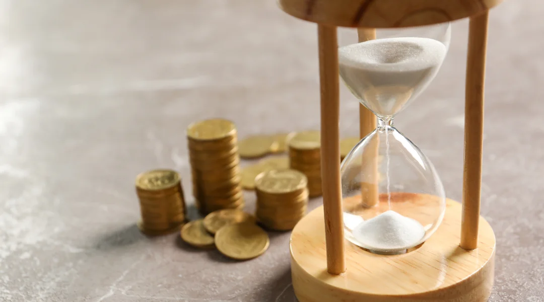 Un sablier rempli de pièces et de sable, symbolisant le temps et l'argent. Prêt rapide 7 jours sur 7.