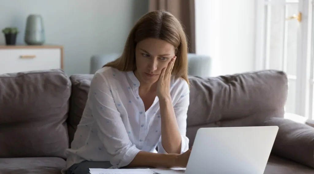 Une femme assise sur un canapé, utilisant un ordinateur portable, illustrant le concept de prêts sur salaire.