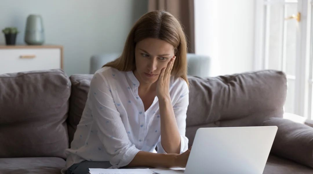 Une femme assise sur un canapé, utilisant un ordinateur portable, illustrant le concept de prêts sur salaire.