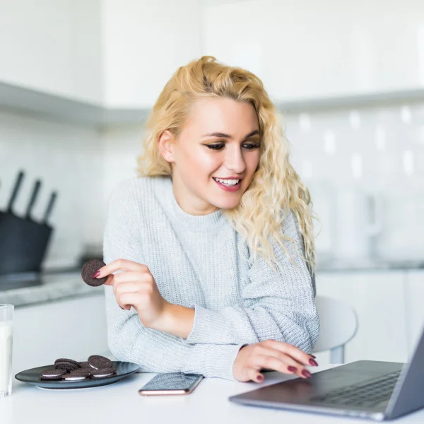 A woman sits at a table with a laptop and a cookie, working on an online loan application.