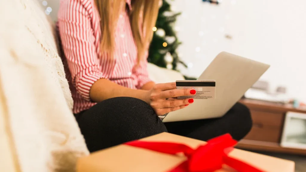 A woman holds a credit card and laptop in front of a decorated Christmas tree, symbolizing holiday loan options.