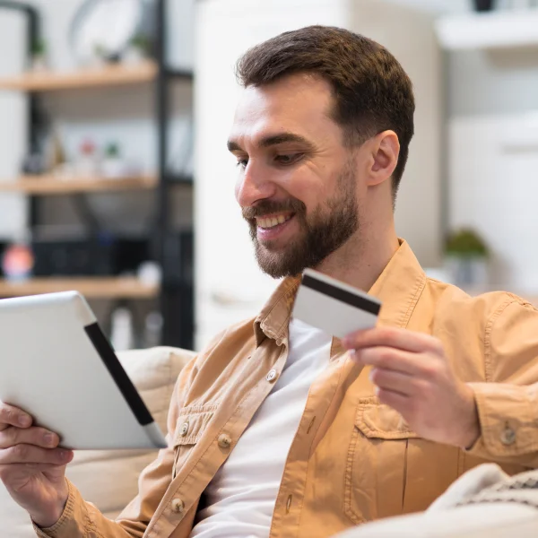 Un homme assis sur un canapé, tenant une tablette et une carte de crédit, explorant des options de prêt personnel.