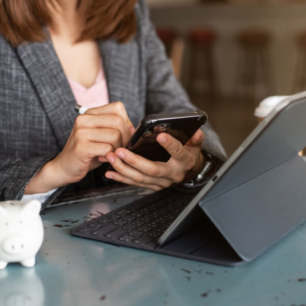 Une femme en costume d'affaires utilise son téléphone, assise à une table avec une tirelire, illustrant les prêts numériques en 2026.